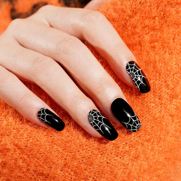 Hand with black nail strips featuring spider web design on an orange textured background
