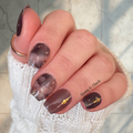 Hand with grey navy and gold foil nail polish and gold accents on a blurred background