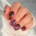 Hand with black and purple glittery nail stickers wearing a white textured sleeve.