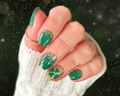 Hand with green nail polish and gold glitter design against a dark background