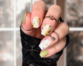 Hand with sunflower nail wraps wearing multiple rings against a blurred background