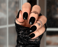 Hand with black nail polish and rings wearing a black textured glove against a blurred background
