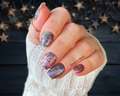 Hand with iridescent nail polish stickers against a dark background