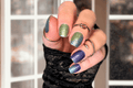 Hand with glittery blue and green nail wraps wearing multiple rings against a blurred background