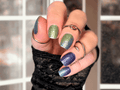 Hand with glittery blue and green nail wraps wearing multiple rings against a blurred background
