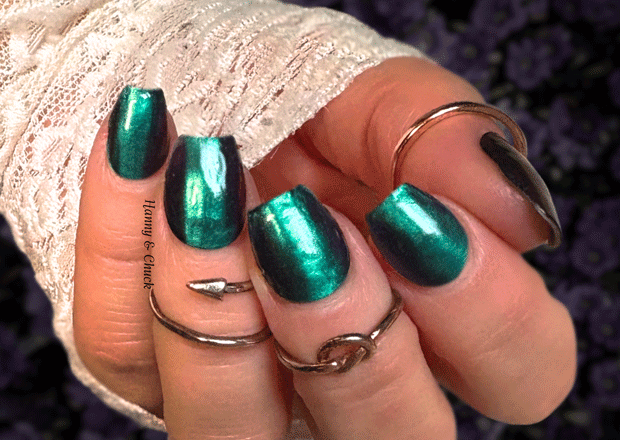 Hand with green metallic nail polish wraps wearing multiple rings on a blurred background