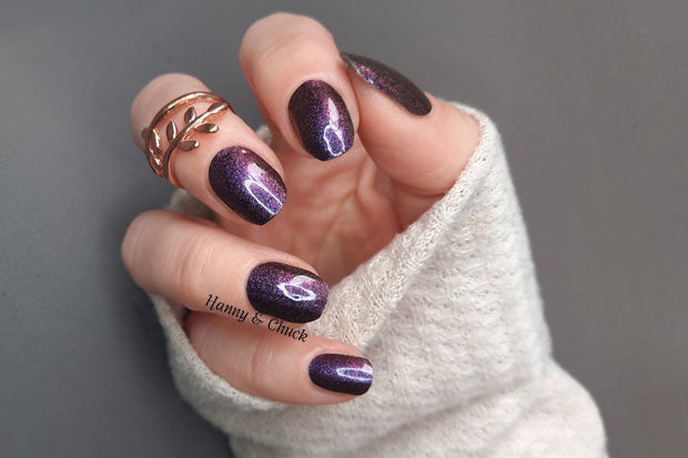 A hand with nail wraps showing a purple and burgundy shimmer with a color-shift effect, turning copper under certain lighting.