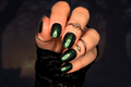 Hand with green glittery nail wraps and multiple rings on a dark background
