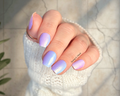 Hand with pastel purple and blue nail wraps on a light background