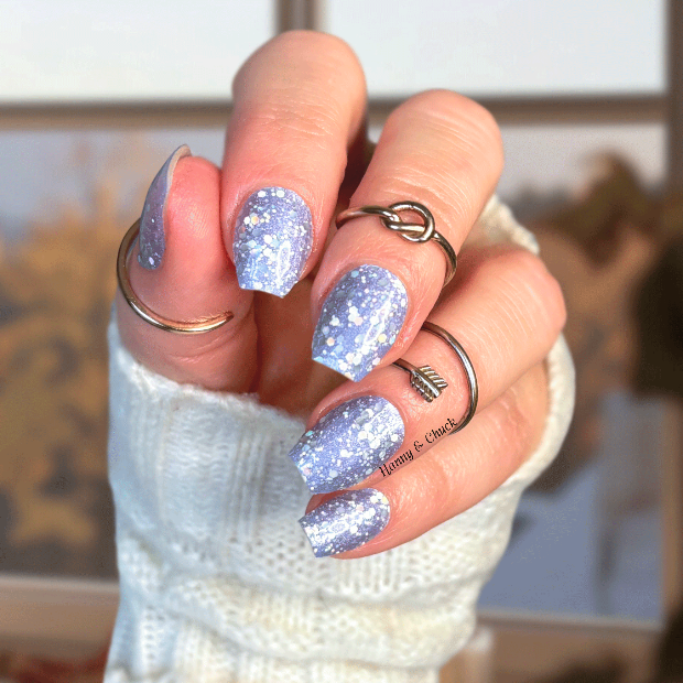 Hand with glittery blue nail polish strips wearing a white sleeve indoors.