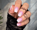 Hand with pink and white gradient nail wraps wearing multiple rings on a neutral backgrounds