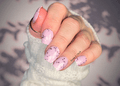 Close-up of a hand with pink nail wraps with pink chunky glitter, wearing a white textured sleeve.