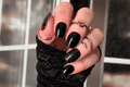 Hand with black nail polish wraps with a black snakeskin accent wrap on the thumb and ring finger. a black glove and multiple rings.