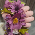 Hand with purple glittery nail polish strips holding a bouquet of purple flowers.