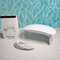 White LED nail lamp with user manual and cable on a marble surface with blue water background