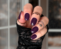 Hand with dark purple nail  wraps wearing black textured sleeve and rings against a blurred background
