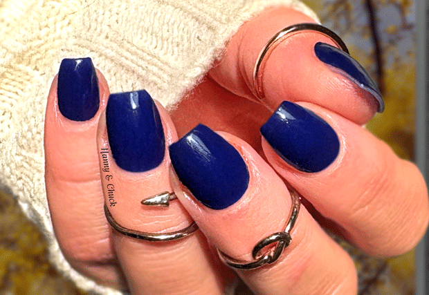 Hand with vibrant blue nail polish wraps wearing multiple silver rings on a blurred background