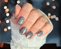 Hand with silver and black leopard print nail wrap design wearing a white textured sleeve.