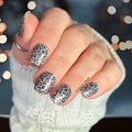 Hand with silver and black leopard print nail strip design wearing a white textured sleeve.