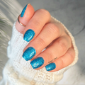 Hand with blue glittery nail polish strips wearing a white sleeve against a neutral background