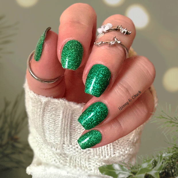 Hand with green glittery nail wraps wearing a white textured sleeve, surrounded by festive decorations.
