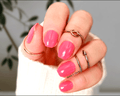 Close-up of a hand with pink nail wraps and multiple rings on a neutral background