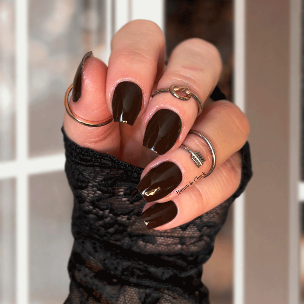 Hand with dark brown nail polish wraps against a blurred indoor background
