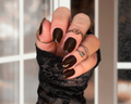 Hand with dark nail wraps and multiple rings against a blurred indoor background