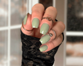 Hand with light green nail wraps wearing black fingerless gloves against a blurred indoor background