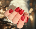 Hand with red glittery nails wearing a white sleeve against a blurred background