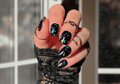 Hand with black glittery nail polish wraps  wearing a textured black sleeve.