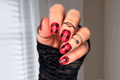 Hand with red and black checkered nail polish wrap design wearing a black sleeve.