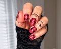 Hand with red and black checkered nail design wearing a black sleeve.