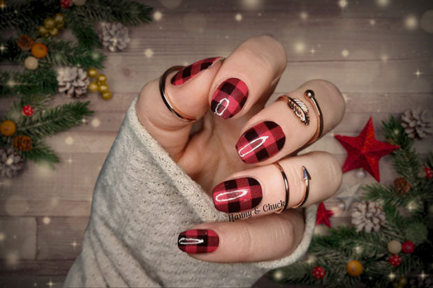 Hand with red and black checkered nail polish wrap design wearing a beige sleeve.