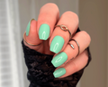 Hand with aqua green nail wraps and black lace sleeve against a neutral background