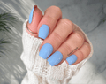 Hand with light blue nail wraps wearing a white textured sleeve against a neutral background