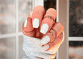 Close-up of a hand with white nail wraps and multiple rings, wearing a textured sleeve.