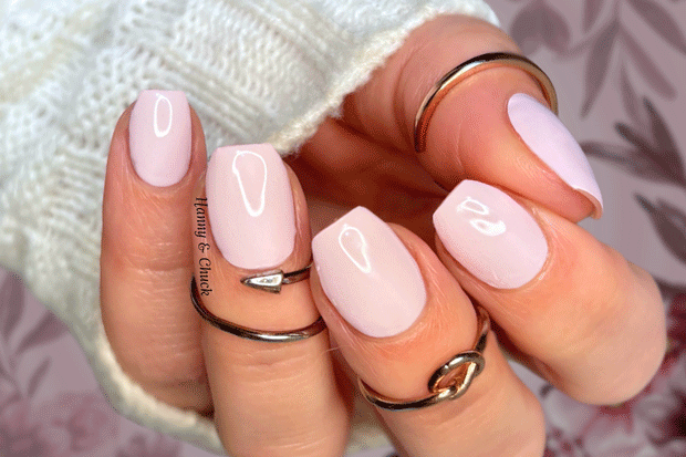 Close-up of a hand with light pink nail polish strips and multiple rings on a patterned background