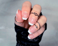 Close-up of a hand with french manicure nail strips and multiple rings on a neutral background