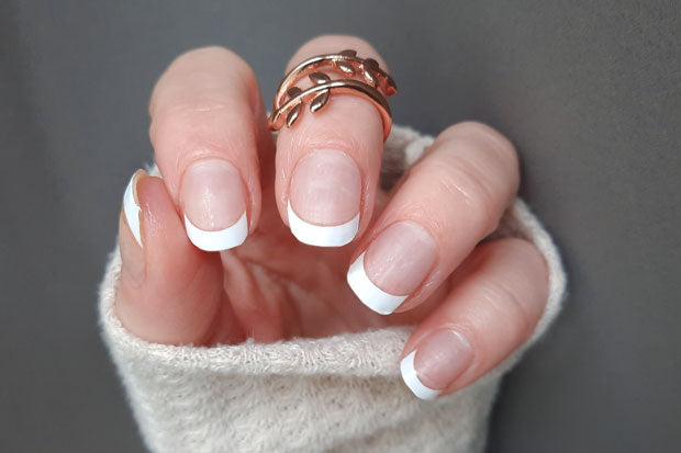 A neatly manicured hand displays a classic French manicure, featuring a clear pink base and crisp, white tips.