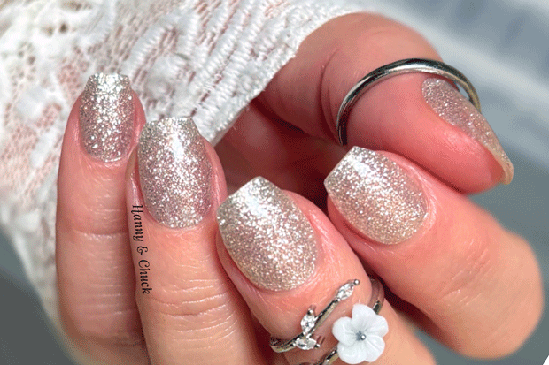 Close-up of a hand with glittery white nail wraps and rings on a blurred background