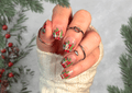 Hand with Christmas-themed nail art wraps in front of a festive background