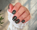 Hand with black and green lucky clover nail wrap design wearing a white textured sleeve.