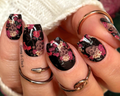 Hand with floral and skull nail wraps wearing multiple rings on a blurred background