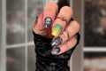 Close-up of a hand with colorful Halloween nail wraps and multiple rings against a blurred background