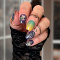 Close-up of a hand with colorful nail art and multiple rings against a blurred background