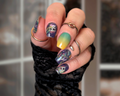 Close-up of a hand with colorful Halloween nail art and multiple rings against a blurred background