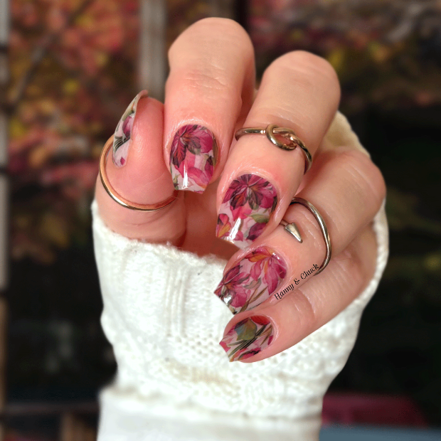 Hand with floral nail wrap design wearing a white textured sleeve against a blurred background