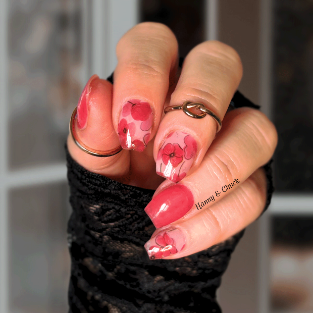 Hand with pink floral nail wrap design wearing a black sleeve, blurred background