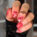 Hand with pink floral nail wrap design wearing a black sleeve, blurred background
